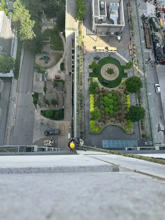 Technician going over the parapet on ropes at the start of a drop, city courtyard far below.