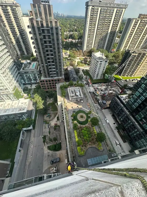 View down a tower from the roof with a roped technician at the edge, showing the working height on a commercial job.