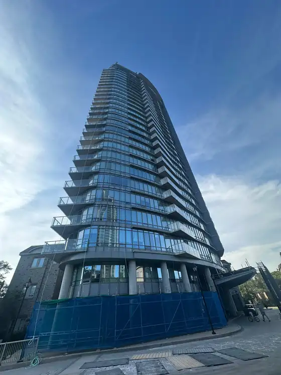 High-rise condominium under exterior sealing work, protective screening wrapped around the podium level.