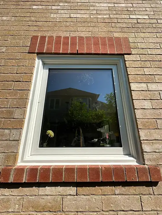 Square window centred between brick soldier courses with a crisp, continuous white perimeter bead in strong sun - the cleanest, best-composed craft shot in this batch.