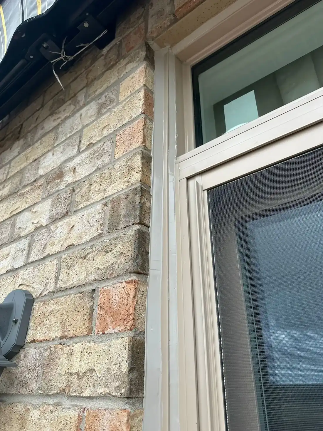 Tight vertical of a thick, straight, freshly tooled sealant bead running the full joint between brick corner and window frame - the cleanest piece of craft in the batch.