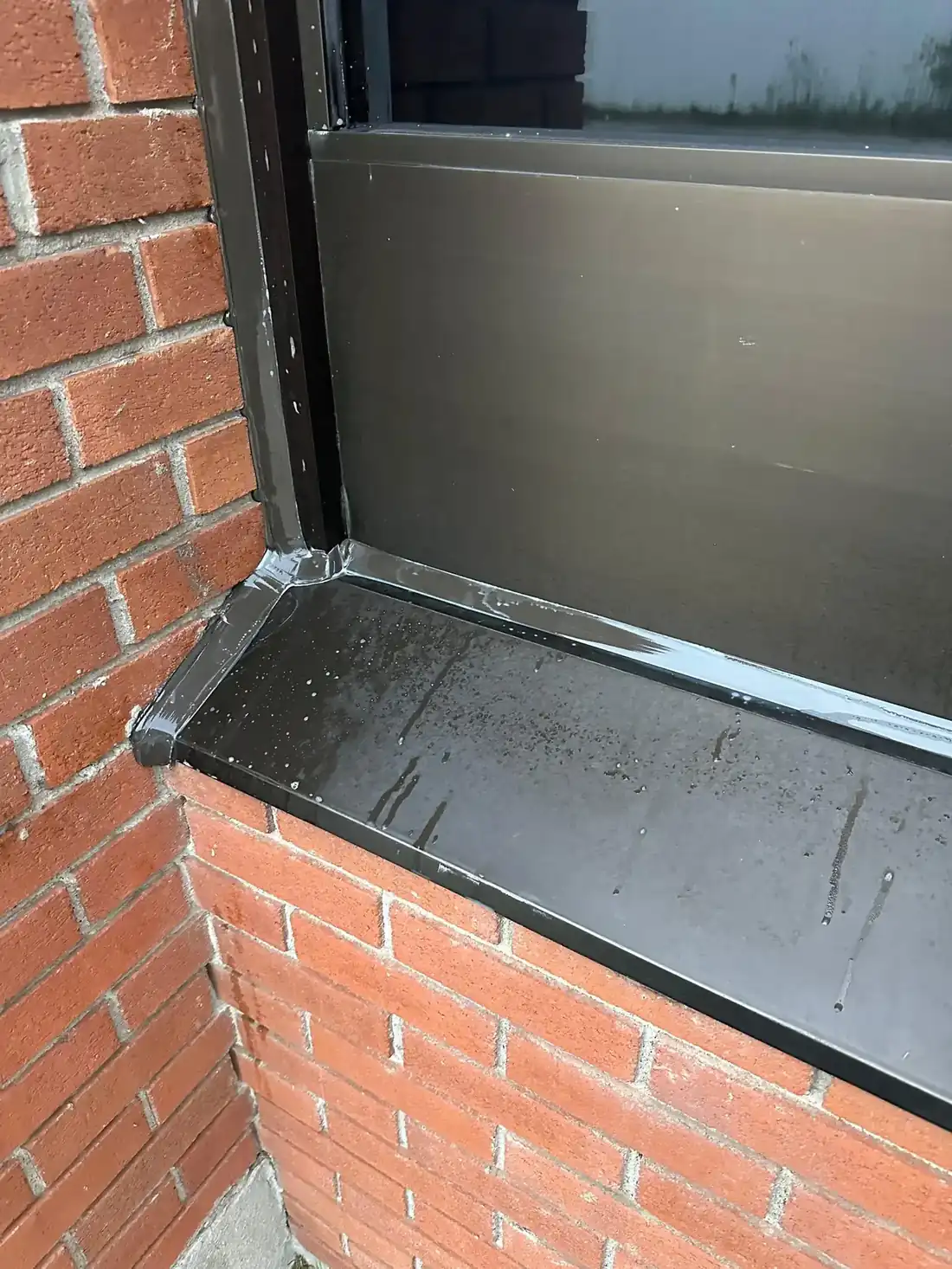 Tight close-up of a window sill and frame corner with a beautifully tooled glossy black bead running the sill joint and turning cleanly at the brick; sharp, well exposed, the single clearest piece of craft in this batch.