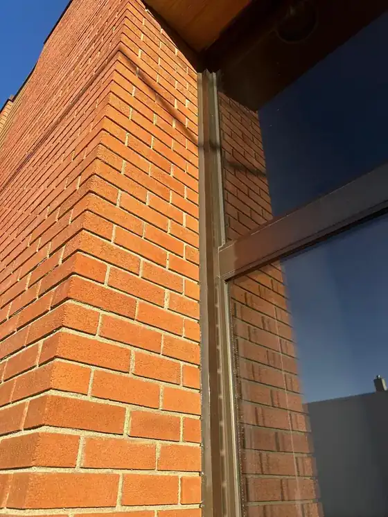 Sunlit red brick corner rising against a deep blue sky with the sealed window frame joint carried up the full height; the most handsome, most usable banner image in the batch.