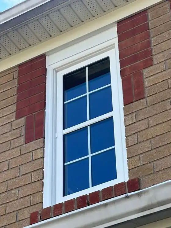 Tall white-trimmed window against two-tone brick with a crisp white perimeter bead and deep blue sky reflected in the glass; strong colour and sharp.