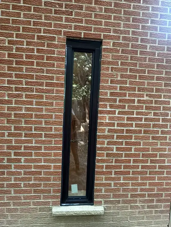 Tall narrow window in brick with a crisp black bead running the full height of both jambs and returning at head and sill; simple and legible.