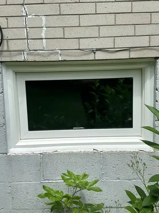 White window in a block wall with a clean white perimeter bead, plus a sealed masonry crack in the wall above - shows both window sealing and crack repair.